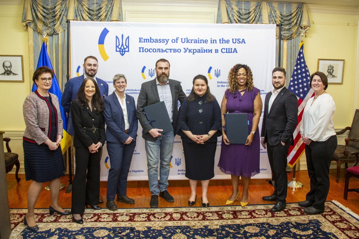 A group of people standing in front of a banner that reads Embassy of Ukraine in the USA in English and Ukrainian