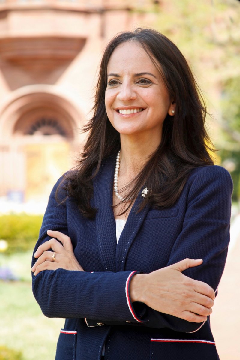 Woman with brown hair and blue blazer snads with her arms crossed in front of the Smithsonian Castle