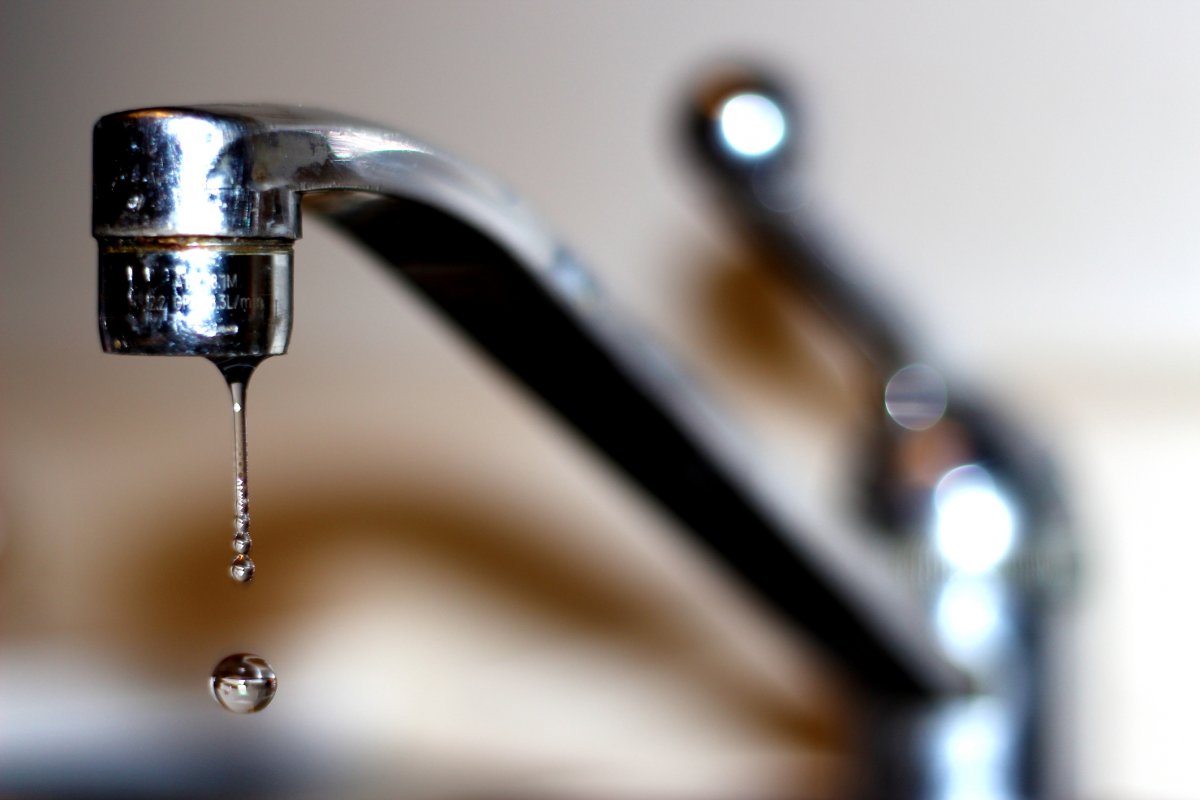 A kitchen faucet with one drop of water coming out.