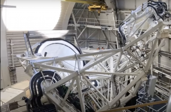Image of the interior of an observatory with white metal structure looking down at the primary mirror of the telescope.