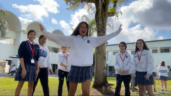 Six middle school girls standing in a half circle in front of a tree with a white school building in the background