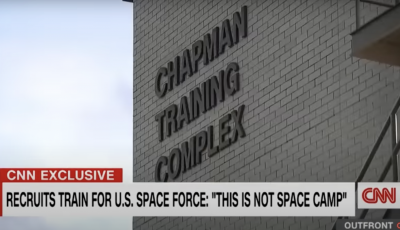 The side of a building with lettering that says Chapman Training Complex and a news title across the bottom that says this is not space camp.