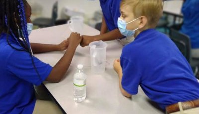 Three students gather around a table with two pitchers of water to work on a science lesson together.