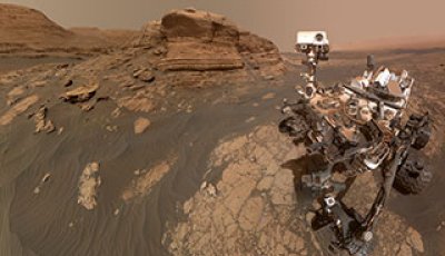 Image of the Martian surface of reddish dust and rock and the rover on the right hand side.