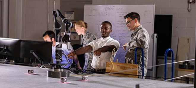 Four people standing in front of two computer screens